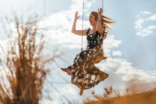 Happy girl with dress enjoying on a swing at sunset