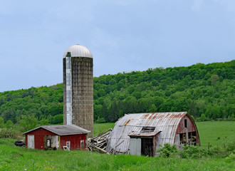 decaying farm shed and silo, with green forested hill