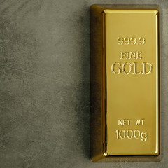 Ingot of pure gold metal bullion on a gray textured background.