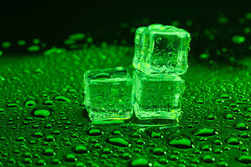 Water drop with ice cubes on lighting green background.