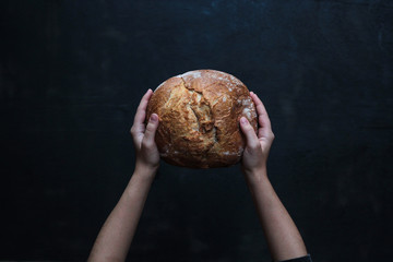 From above tasty appetizing loaf of bread in hands on black background