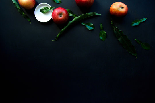 From above bright red appetizing apples with green leaves and white small plate on black background