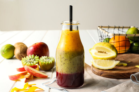 Glass bottle with layers of delicious fruit smoothie with straw placed on white table