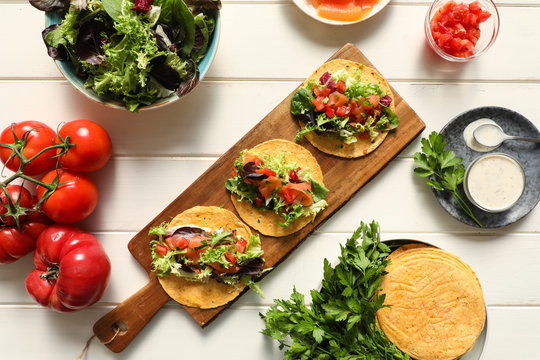 From above wooden cutting board with tasty vegetarian tacos placed on white tabletop