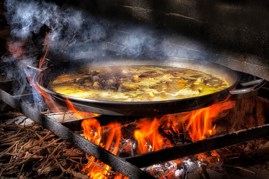 Big iron pan with boiling broth for cooking paella over open fire with wood