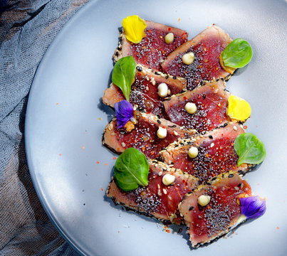 From above delicious appetizing fresh tuna tataki with green leaves on plate