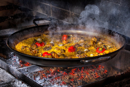 Hot delicious paella with rice, chicken and vegetables cooked in iron pan over open fire