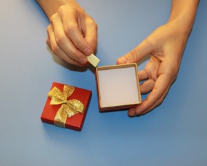 Valentine's Day hands holding a red gift box with a gold shiny bow and a paper note sheet