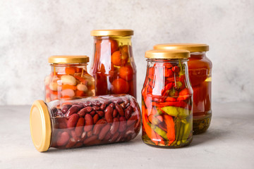 Jars with different canned vegetables and beans on grey table
