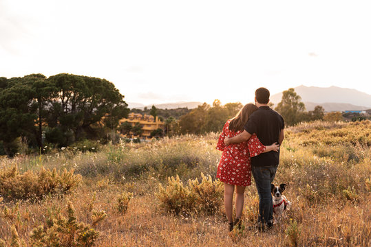 Back view of unrecognizable couple having fun with a little dog among high grass in countryside while admiring the views