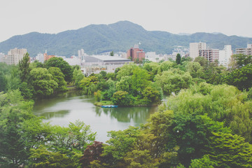Fototapeta na wymiar Tropical view of Nakajima Park (Koen) with cityscape of Sapporo City in the background at Hokkaido, Japan