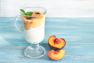 Glass of yogurt with slices of sweet ripe juicy fruit, peaches with green leaves in a basket on white background