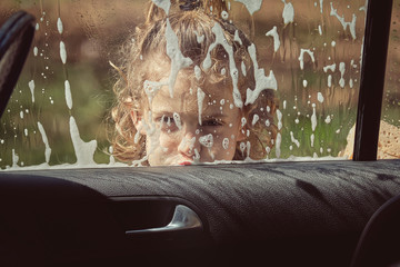 Child washing front glass of car by hand