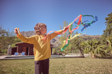 Happy kid playing with colorful kite flying in blue sky near wood cabin on nature background