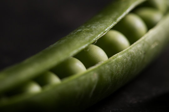 Peeled fresh peas and pea pods on dark background