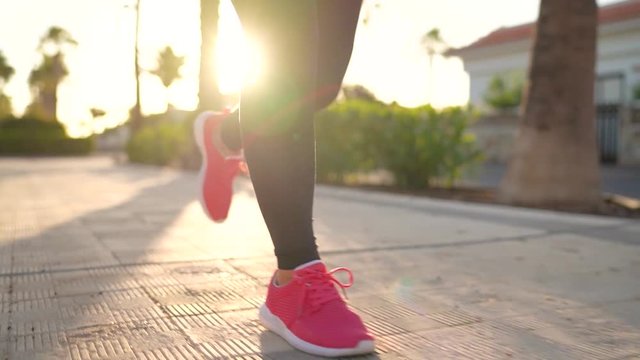 Close up of legs of a woman running along the palm avenue at sunset