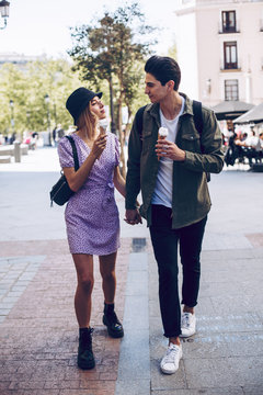 Cheerful young attractive woman and boyfriend walking holding hands while eating cornet of ice cream outdoors