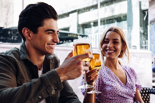 Cheerful young attractive couple enjoying refreshing drink during walking in town in warm day