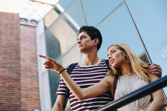 Attractive young couple of tourists admiring view while standing in front of modern building