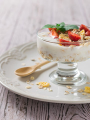 Yogurt with berries and mint on a wooden table with a spoon.
