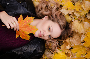 Beautiful woman lying on yellow leaves in park. Leisure time on warm autumn day