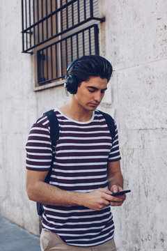 Attractive young man in casual clothes listening music during walking on street in daylight