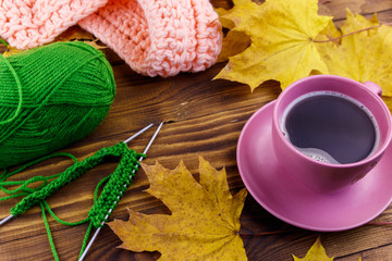 Cup of coffee, ball of yarn, knitting, knitted scarf and yellow maple leaves on wooden table. Autumn still life