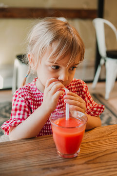 Appetizing fragrant glass of red smoothie in hands of adorable child drinking it at table