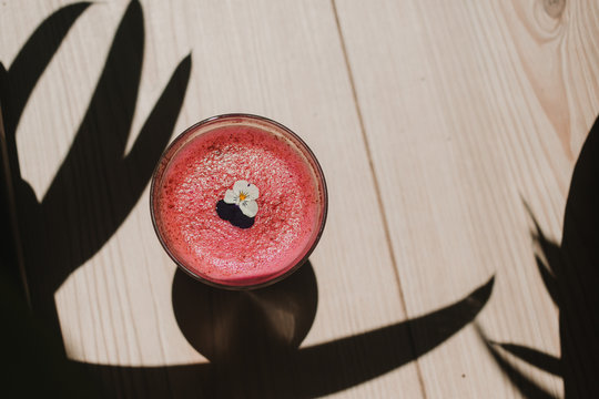 From above bubble frothy tasty fragrant pink smoothie with flowers in glass on wooden table