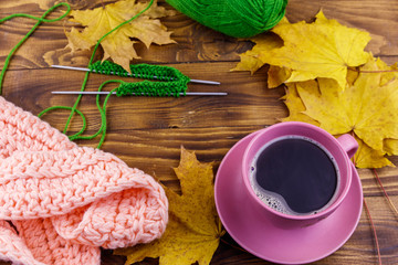 Cup of coffee, ball of yarn, knitting, knitted scarf and yellow maple leaves on wooden table. Autumn still life