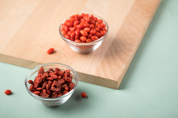 Frische und getrocknete Goji-Beeren Superfood in Glas Schale auf Holz Brett und Mint Grün Pastell Hintergrund