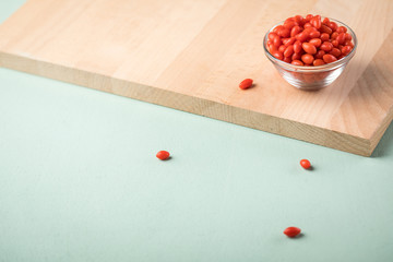Frische Goji-Beeren Superfood in Glas Schale auf Holz Brett und Mint Grün Pastell Hintergrund