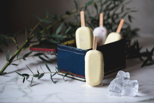 Assorted ice cream popsicles inside a vintage metallic box placed on a marble surface decorated with flowers
