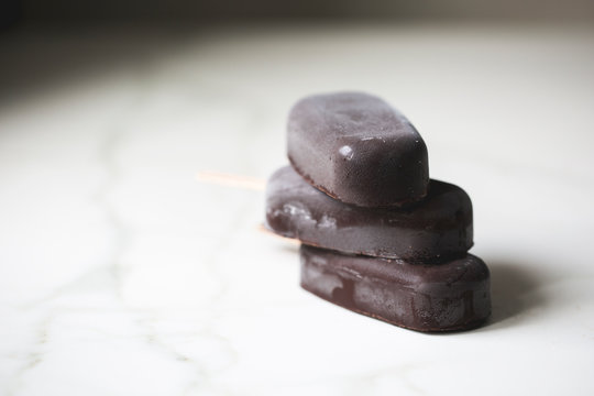 Several chocolate ice cream popsicles stacked on a marble surface