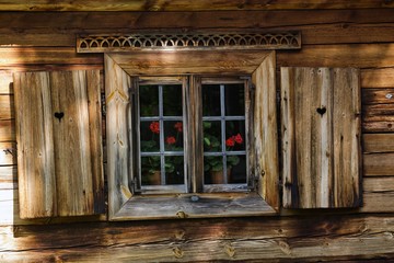 Drewniany dom z drewnianymi okiennicami, ozdobami i pelargoniami w oknach - obrazy, fototapety, plakaty