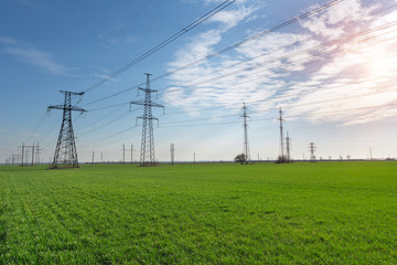 High-voltage power lines passing through a green field, on the background of a beautiful cloudy sky