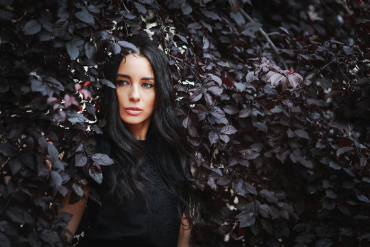 beautiful woman in black dress in the leaves in the garden