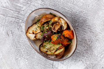 Plate of grilled vegetables - potato, pumpkin and mushrooms at concrete textured background.
