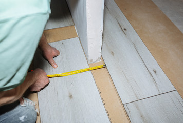 Worker making laminate flooring in apartment. Measure tape and pencil in hands. Maintenance repair renovation. Wooden parquet planks indoors.