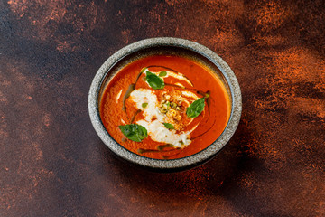 Plate of tomato gaspacho soup served with nuts at concrete textured table background.