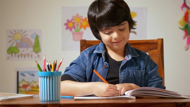 Little Indian boy sitting in his study room and studying - Drawing a picture.Childhood. Young charming boy drawing and coloring in a book at home - art and craft skills