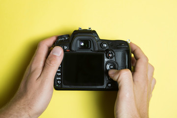 Digital Single Lens Reflex on yellow background, screen off view from above. Hand touching the...