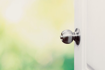 Door knobs open and the white door opening with natural bokeh backdrop.