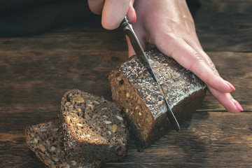 Woman is cutting a fresh bread by a kitchen knife on a cutting board.
