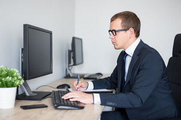 handsome businessman using computer and writing something on clipboard