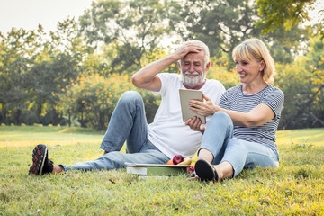 Elderly couple is sitting on a tablet in the park.
