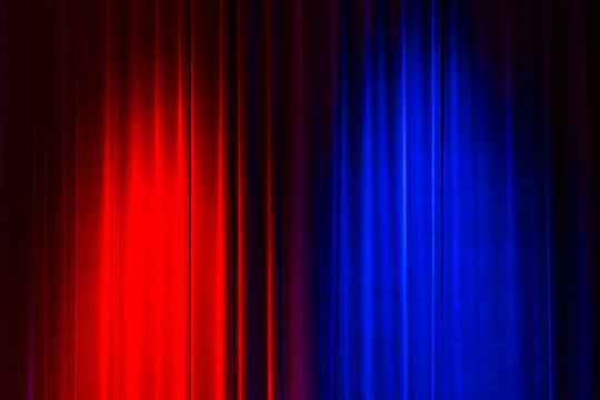 Front view of a closed vintage style velvet theater curtain illuminated by a red and a blue spotlight