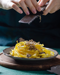 Female hands grating parmesan cheese, black truffle onto pasta tagliatelle.