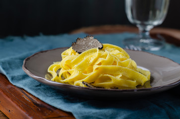 Italian cuisine- tagliatelle with black truffle on rustic plate.