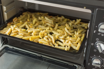 Oven baked potato sticks. French fries inside an oven. Fast food potato skins on a baking tray. Seasoned potato sticks.